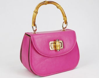 Könnte beinhalten: Eine kleine rosa Lederhandtasche mit einem Bambus-Oberhenkel und einem goldenen Verschluss.