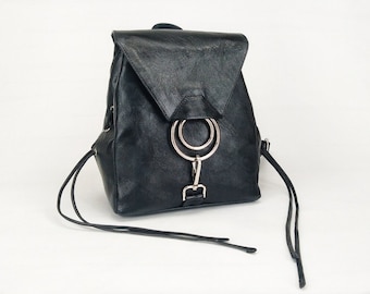 Könnte beinhalten: Schwarzer Lederrucksack mit Klappenverschluss und silbernem Metallringdetail. Der Rucksack hat verstellbare Träger und einen Kordelzugverschluss. Die Tasche befindet sich auf weißem Hintergrund.