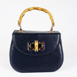 K&ouml;nnte beinhalten: Eine dunkelblaue Ledertasche mit einem Bambusgriff und einem goldenen Verschluss.