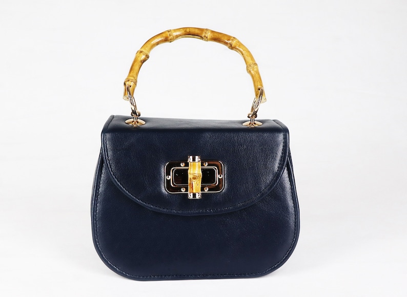 K&ouml;nnte beinhalten: Eine dunkelblaue Ledertasche mit einem Bambusgriff und einem goldenen Verschluss.