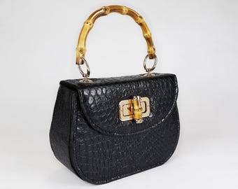 Könnte beinhalten: Eine schwarze Handtasche aus krokodilgeprägtem Leder mit einem Bambus-Obergriff und goldenen Beschlägen.