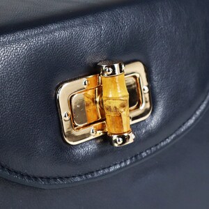 K&ouml;nnte beinhalten: Eine dunkelblaue Ledertasche mit einem goldenen Verschluss und einem Bambus-Knopf.