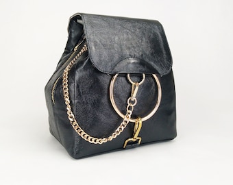 Könnte beinhalten: Schwarzer Lederrucksack mit einer goldenen Kette und einem großen goldenen Ringdetail.