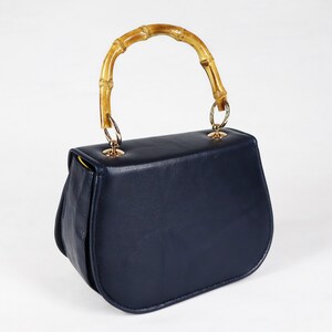 K&ouml;nnte beinhalten: Eine dunkelblaue Ledertasche mit einem Bambusgriff und goldenen Beschl&auml;gen.
