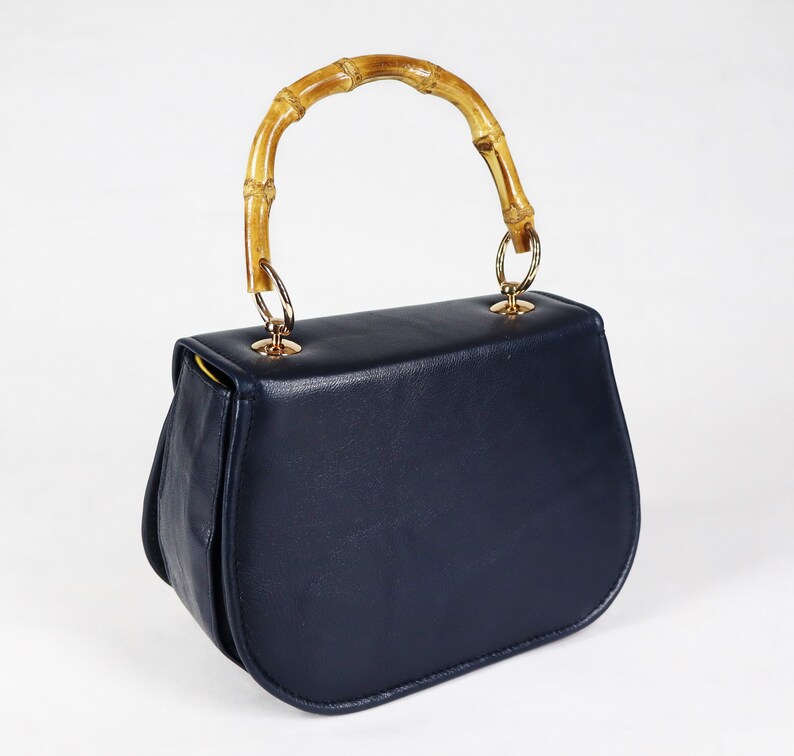 K&ouml;nnte beinhalten: Eine dunkelblaue Ledertasche mit einem Bambusgriff und goldenen Beschl&auml;gen.