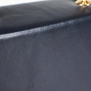 K&ouml;nnte beinhalten: Eine dunkelblaue Ledertasche mit goldfarbenem Henkel und Beschl&auml;gen.