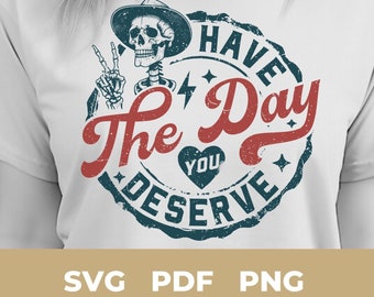 May include: A white t-shirt with a blue and red graphic design. The graphic features a skeleton wearing a cowboy hat and holding a peace sign. The text reads "Have the Day You Deserve".