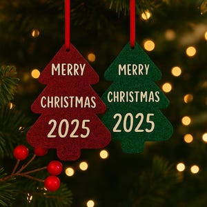 May include: Two Christmas tree decorations, one red and one green, shaped like trees. Each has the words "MERRY CHRISTMAS 2025" in white. They hang from red ribbons against a backdrop of festive lights and foliage.