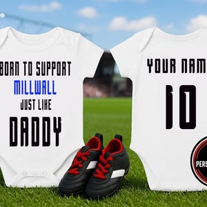 Pode incluir: Dois bodies brancos para bebé com texto preto. Um diz "BORN TO SUPPORT MILLWALL JUST LIKE DADDY" e o outro tem "YOUR NAME" e o número "10". Botas de futebol pretas e vermelhas estão à frente.