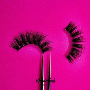 Könnte beinhalten: Zwei Paar falsche Wimpern auf einem rosa Hintergrund. Die Wimpern sind schwarz und haben einen natürlichen, federleichten Look. Der Text "Wonderlash London" ist unten in der Mitte des Bildes sichtbar.