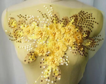 May include: A yellow floral applique with gold sequins and pearl beads. The applique is on a sheer yellow fabric.