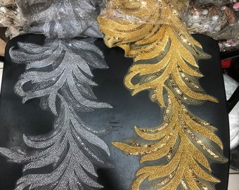 May include: Two beaded fabric trims, one silver and one gold, with a feather-like design. The trims are on a black surface.