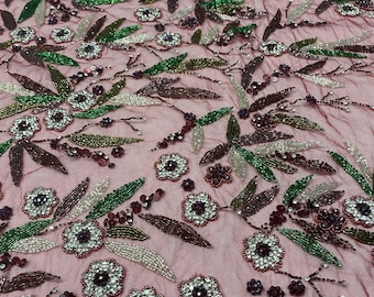 May include: Pink mesh fabric with beaded floral embroidery. The flowers are made with white, green, and purple beads. The fabric has a delicate, feminine look.