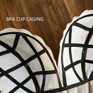 Op de afbeelding: Close-up van een witte bh-cup van stof met zwarte elastische bandjes. De tekst "BRA CUP CAGING" is zichtbaar bovenaan de afbeelding.