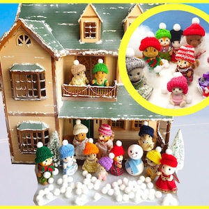 Puede incluir: Un grupo de pequeñas figuritas de animales coloridas que llevan gorros de punto y juegan en la nieve frente a una casa de muñecas. Las figuritas sostienen bolas de nieve y un muñeco de nieve está en el centro del grupo.