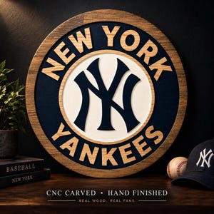 May include: A circular wooden wall sign featuring the New York Yankees logo in navy blue and white. The text NEW YORK YANKEES is carved in wood lettering around the central logo. The sign has a natural wood frame and a dark navy blue background.