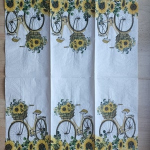 Puede incluir: Una servilleta de papel blanca con un patr&oacute;n repetido de girasoles amarillos y una bicicleta con una cesta llena de girasoles.