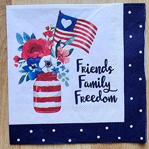 May include: A white paper napkin with a red, white and blue striped mason jar filled with red, white and blue flowers. The jar has a red, white and blue striped lid. An American flag with a white heart in the top left corner is behind the flowers. The text "Friends Family Freedom" is printed on the napkin.