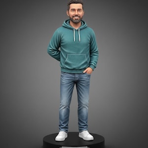 May include: A figurine of a person with a beard, wearing a teal hooded sweatshirt with white drawstrings, blue denim jeans, and white sneakers. The figure stands on a round black base featuring a silver nameplate with the text LIAM engraved.
