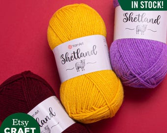 Pode incluir: Três novelos de lã em cores diferentes: bordô, amarelo e roxo. Cada novelo tem uma etiqueta branca com o texto "Shetland" e uma pequena ilustração de ovelha. A etiqueta também inclui o texto "YarnArt". O fundo é vermelho. O texto "TODAS AS CORES EM ESTOQUE!" está em verde.