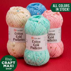 Peut inclure: Cinq pelotes de fil YarnArt Cotton Gold Paillettes, aux couleurs crème, bleu, rose et turquoise, ornées de paillettes scintillantes. L'image contient le texte "TOUTES LES COULEURS EN STOCK !" et le nom de la boutique Etsy "CRAFT MAXI SHOP".