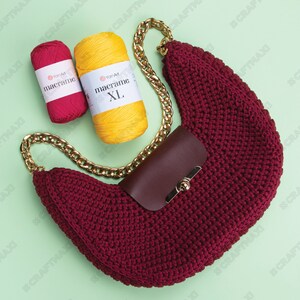 May include: A maroon crocheted handbag with a gold chain strap and a brown leather flap with a gold clasp. Two balls of yarn are in the background, one red and one yellow, both labeled "YarnArt macrame".