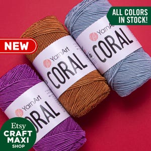May include: Three skeins of yarn in different colors: purple, orange, and blue. The yarn is labeled "YarnArt Coral" and says "All Colors In Stock!"