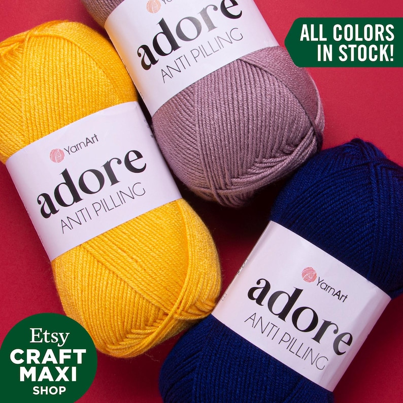 Three skeins of YarnArt Adore anti-pilling yarn in yellow, mauve, and navy.