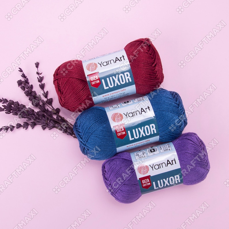 May include: Three balls of yarn in red, blue, and purple. Each ball has a label that says "YarnArt Luxor Giza Cotton" and includes the website address www.yarnart.info.