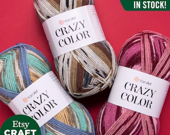 May include: Three balls of YarnArt Crazy Color yarn in different colour combinations. The balls are on a red background. The text "ALL COLORS IN STOCK!" is in a green box above the balls.