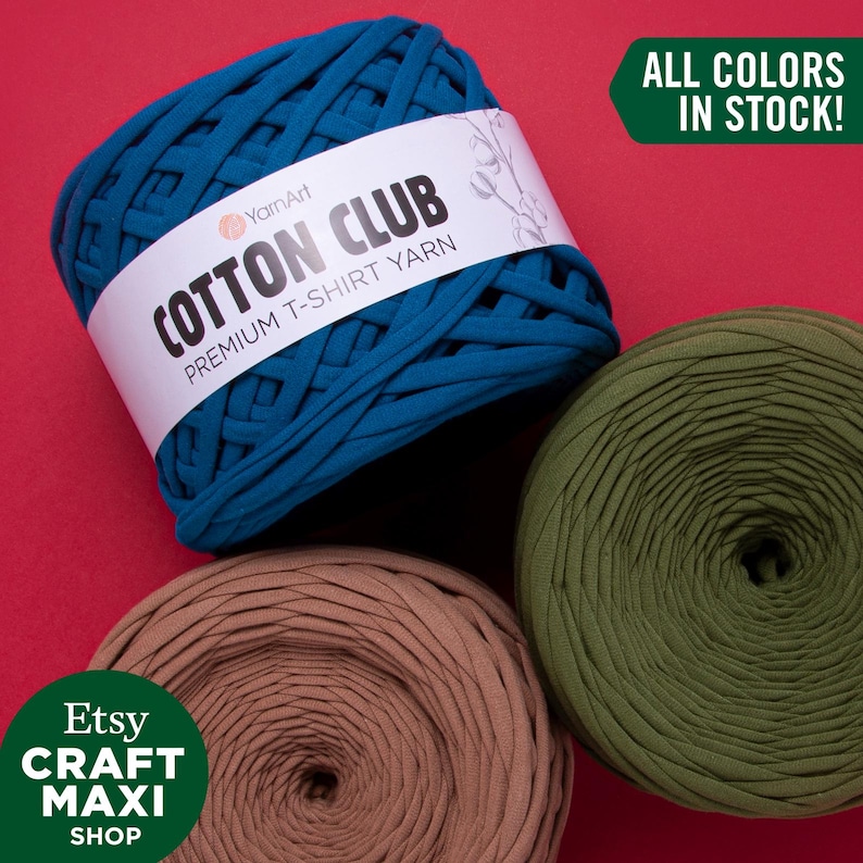 May include: Three spools of yarn in teal, brown, and green. The yarn is made of cotton and is labeled "Cotton Club Premium T-Shirt Yarn". The text "All Colors In Stock!" is in a green box.