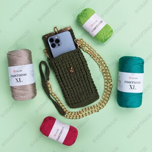 May include: A green crocheted phone case with a gold chain strap. Four balls of yarn in different colors are arranged around the case. The yarn labels read "macrame XL" in white text.