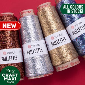 May include: Four spools of YarnArt Paillettes yarn in silver, gold, copper, and blue. The yarn is sparkly and has a metallic sheen. The spools are labelled with the YarnArt logo and the text "Paillettes". The text "ALL COLORS IN STOCK!" is displayed in green letters on a white background. The text "NEW" is displayed in red letters on a white background.
