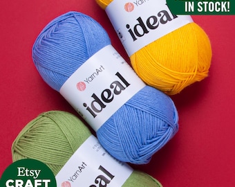 Może przedstawiać: Trzy motki przędzy YarnArt Ideal w kolorze niebieskim, żółtym i zielonym, z białymi etykietami. Widoczny jest tekst "ALL COLORS IN STOCK!". Logo Etsy Craft Maxi Shop znajduje się w lewym dolnym rogu. Przędza leży na czerwonym tle.