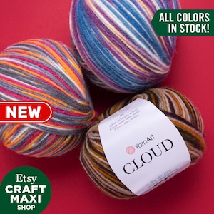 以下が含まれることがあります： 異なる色の組み合わせで、YarnArt Cloud 糸の糸巻きが3つあります。糸は、茶色、オレンジ、灰色、ピンク、青、白の混合です。糸巻きは赤い背景の上にあります。1つの糸巻きのラベルには「YarnArt Cloud」と「全色在庫あり！」というテキストが書かれています。