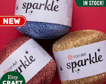 Op de afbeelding: Drie bollen glinsterend garen in blauw, rood en goud. Het garen is gelabeld "YarnArt sparkle" en er staat "Alle kleuren op voorraad!"