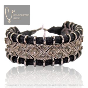 Könnte beinhalten: Ein schwarz-silbernes Armband mit einem rautenförmigen Muster. Das Armband hat eine schwarze Kordelbasis mit silbernen Akzenten und diamantbesetzten Abschnitten. Der Schmuck wird auf einer weißen Oberfläche präsentiert.