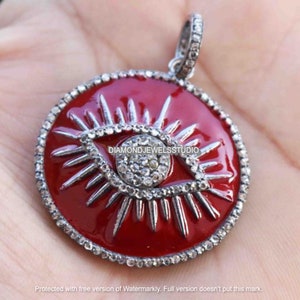 May include: A circular, red pendant featuring a silver-coloured eye design. The eye is detailed with small, sparkling stones and surrounded by rays. The pendant has a silver-coloured border and a loop for a chain.