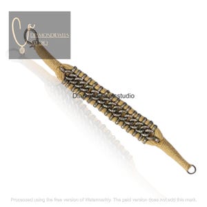 May include: A tan and silver bracelet with a woven design. The bracelet features a series of silver links adorned with small, sparkling stones, creating a textured pattern. The ends of the bracelet are finished with a looped closure.