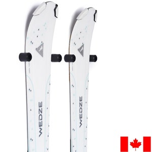 May include: Two white skis with black ski poles mounted on a white wall. The skis have a blue and white pattern and the text "WEDZE" printed on them.