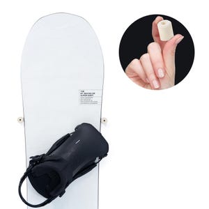 May include: A white snowboard with black bindings. The board features the text "THE MT. BACHELOR SUPER EIGHT". A small, cylindrical, off-white object is held between two fingers in a circular inset.