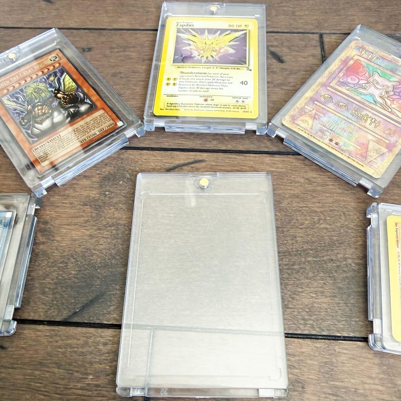 May include: Several trading cards in clear plastic holders are arranged on a wooden surface. The cards feature various characters and designs, including a yellow and purple bird-like creature and a blue-haired warrior.