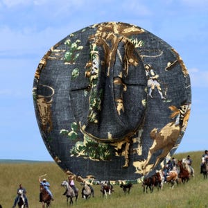 Puede incluir: Un sombrero de vaquero con una base de denim negro y un estampado colorido de vaqueros montando a caballo. El estampado presenta una gama de colores verde, marr&oacute;n y amarillo.