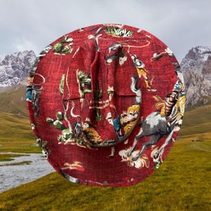 Puede incluir: Un sombrero de vaquero rojo con un estampado de tem&aacute;tica western que presenta vaqueros, caballos y cactus. El sombrero est&aacute; hecho de una tela tejida y tiene un ala ancha.