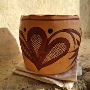 May include: A terracotta pot with a brown and black geometric design. The pot is decorated with a stylised floral pattern.