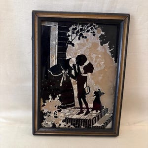 May include: Framed vintage silhouette art depicting a mother and child with a dog. The black and white artwork shows a mother holding a child, with a dog standing nearby. The frame is a dark brown color.
