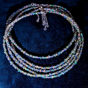 May include: A multi-strand necklace made of iridescent opal beads. The necklace is silver and has a heart-shaped clasp.