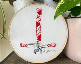 May include: Embroidered hoop art featuring a stylized image of a spaceship with red flowers and the text "flylo rem".