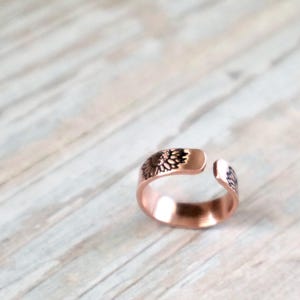 May include: A copper ring with a floral design. The ring is open on one side and has a smooth, polished finish.