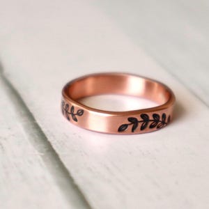 May include: A copper band ring with a delicate floral design etched into the surface.